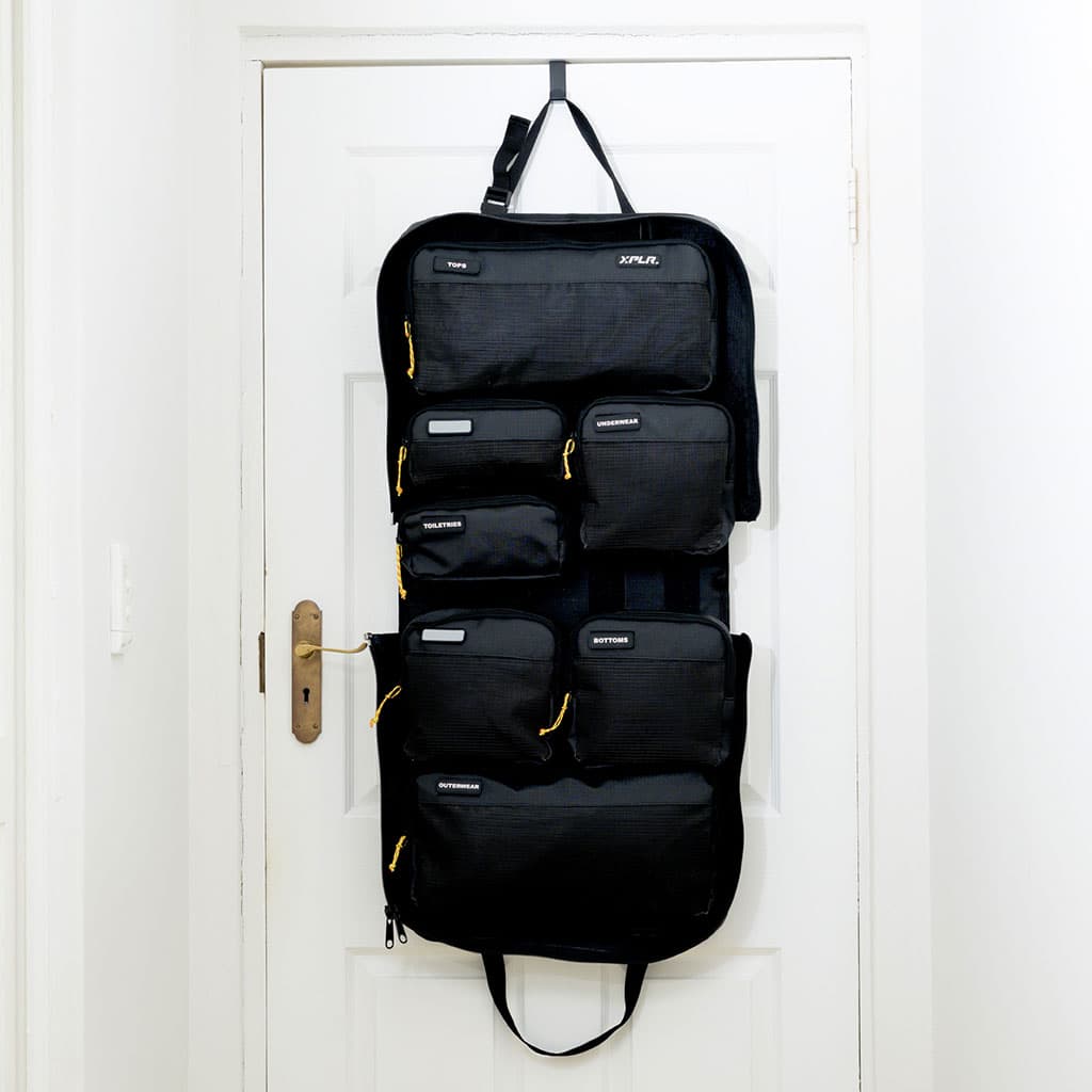 Woman accessing the XPLR duffel hanging from a door hook, showing all compartments open and organized